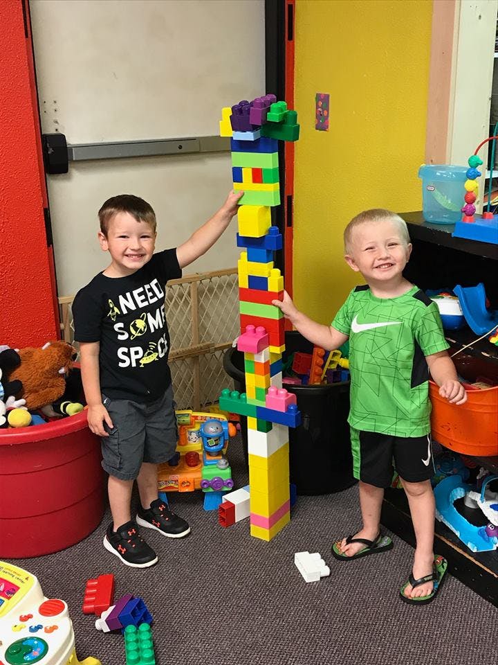 Two children standing next to a tall tower built from colorful blocks