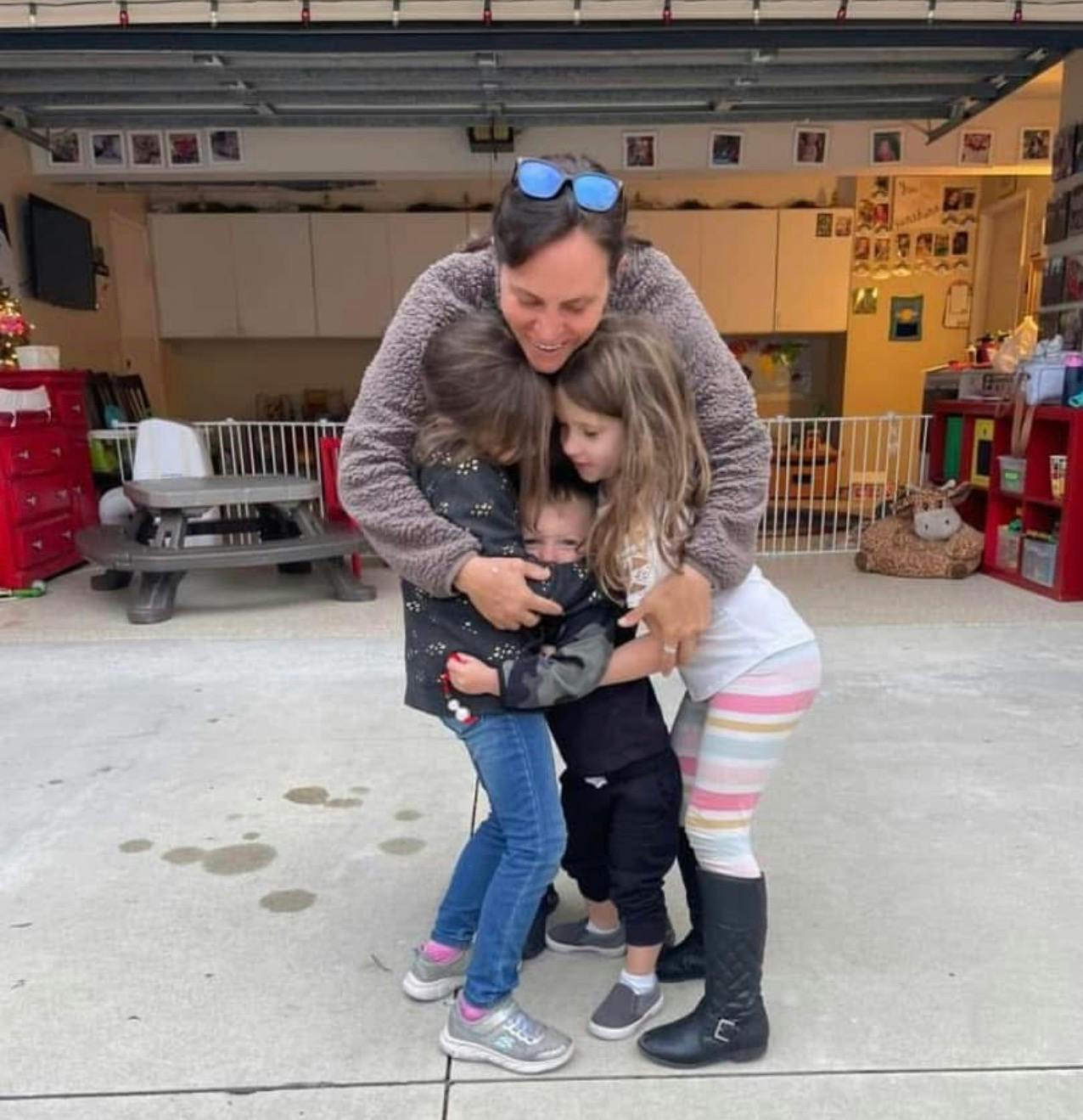 Person embracing three children in a group hug