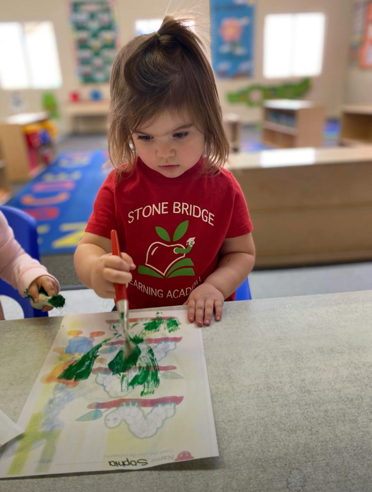 Child painting with green paint on paper in a classroom