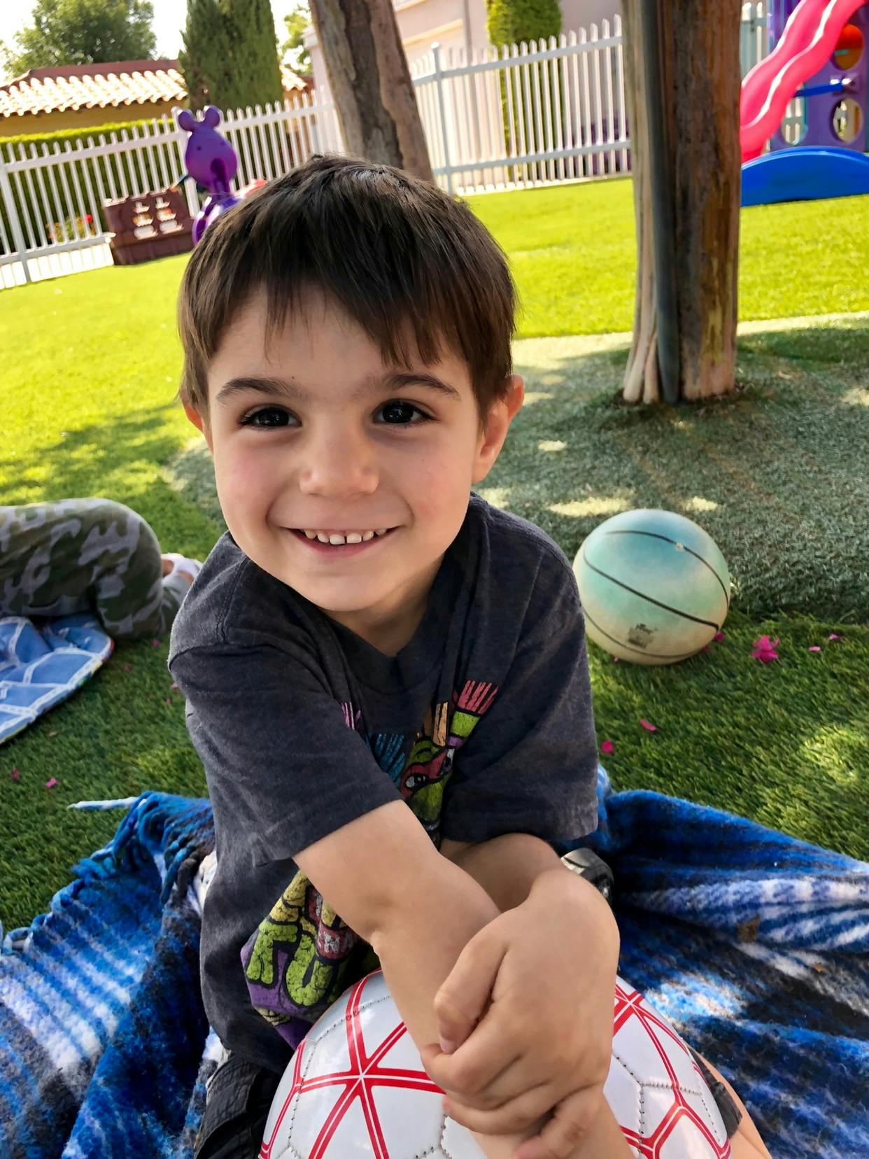 Child sitting on a blanket with a soccer ball in a grassy area