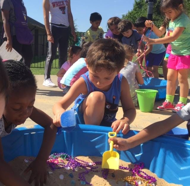 Children playing in a sandbox with shovels and beads