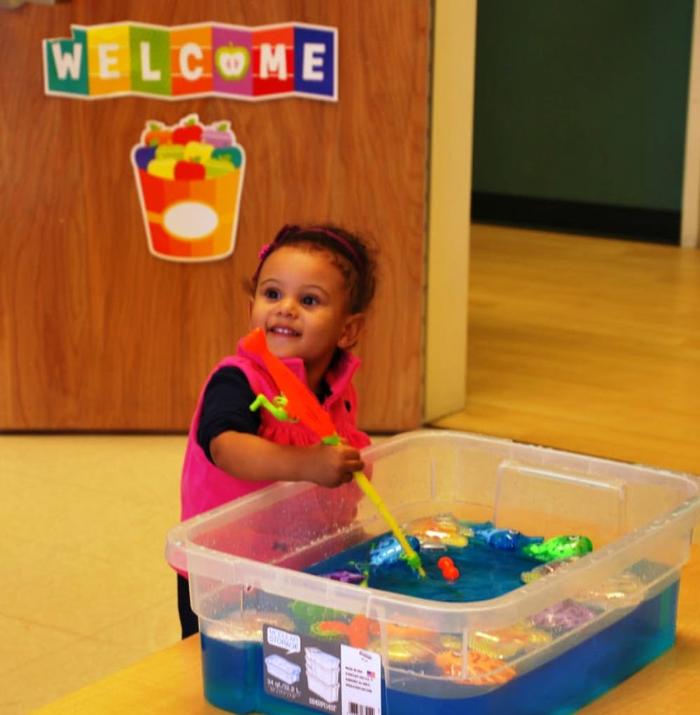 Child playing with a fishing toy in a water bin