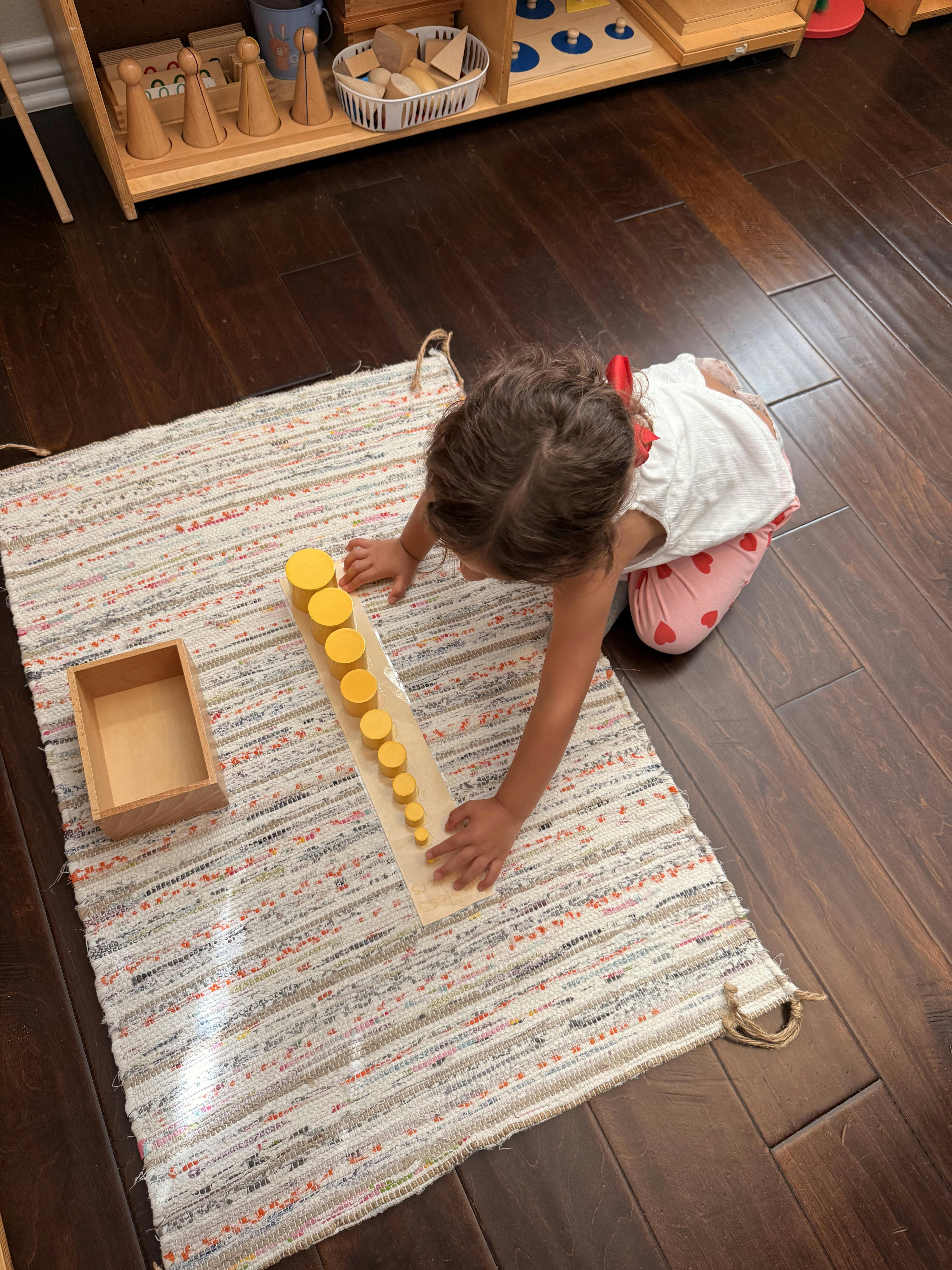 Child playing with yellow cylinder blocks on a rug