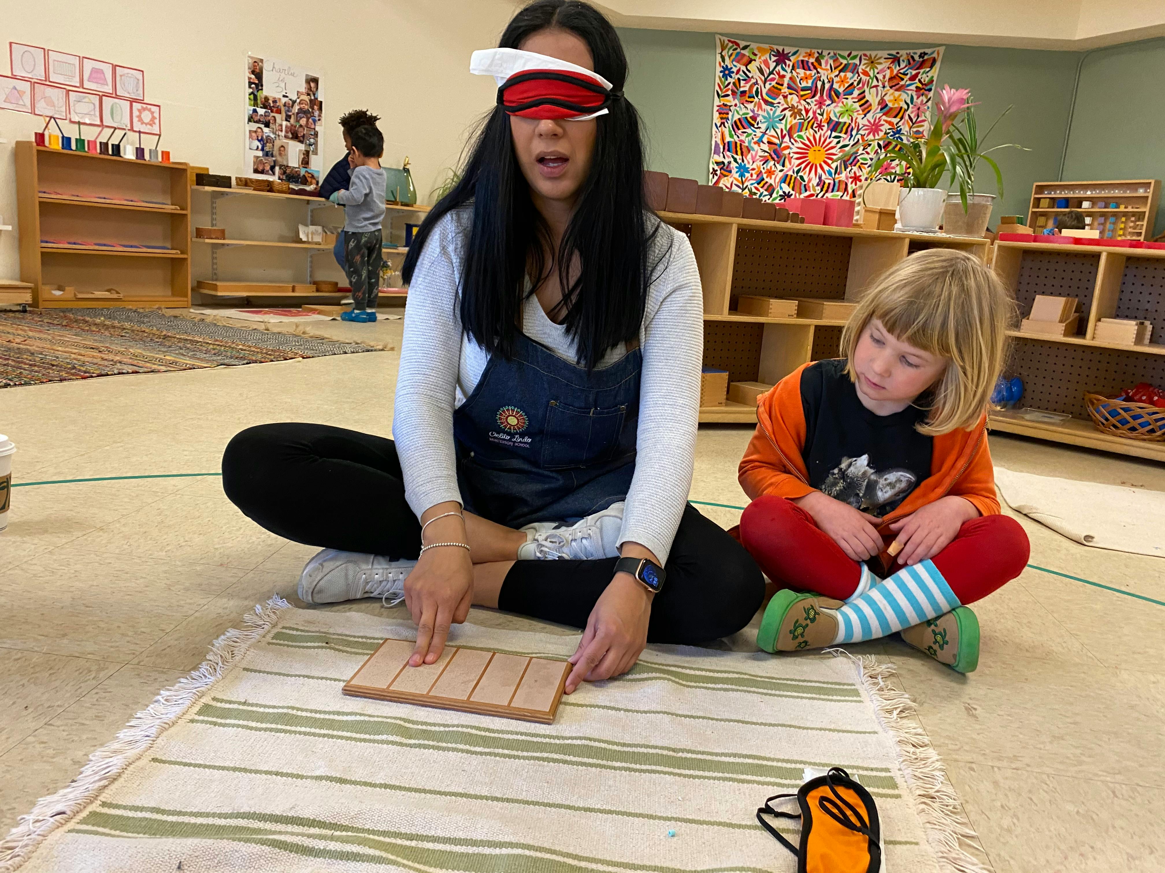 Person blindfolded pointing at a wooden block while a child watches