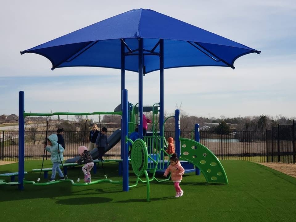 Children playing on a playground with a large blue shade structure