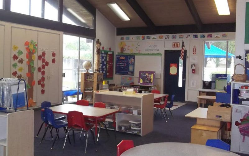An empty classroom with small tables and chairs, and learning materials