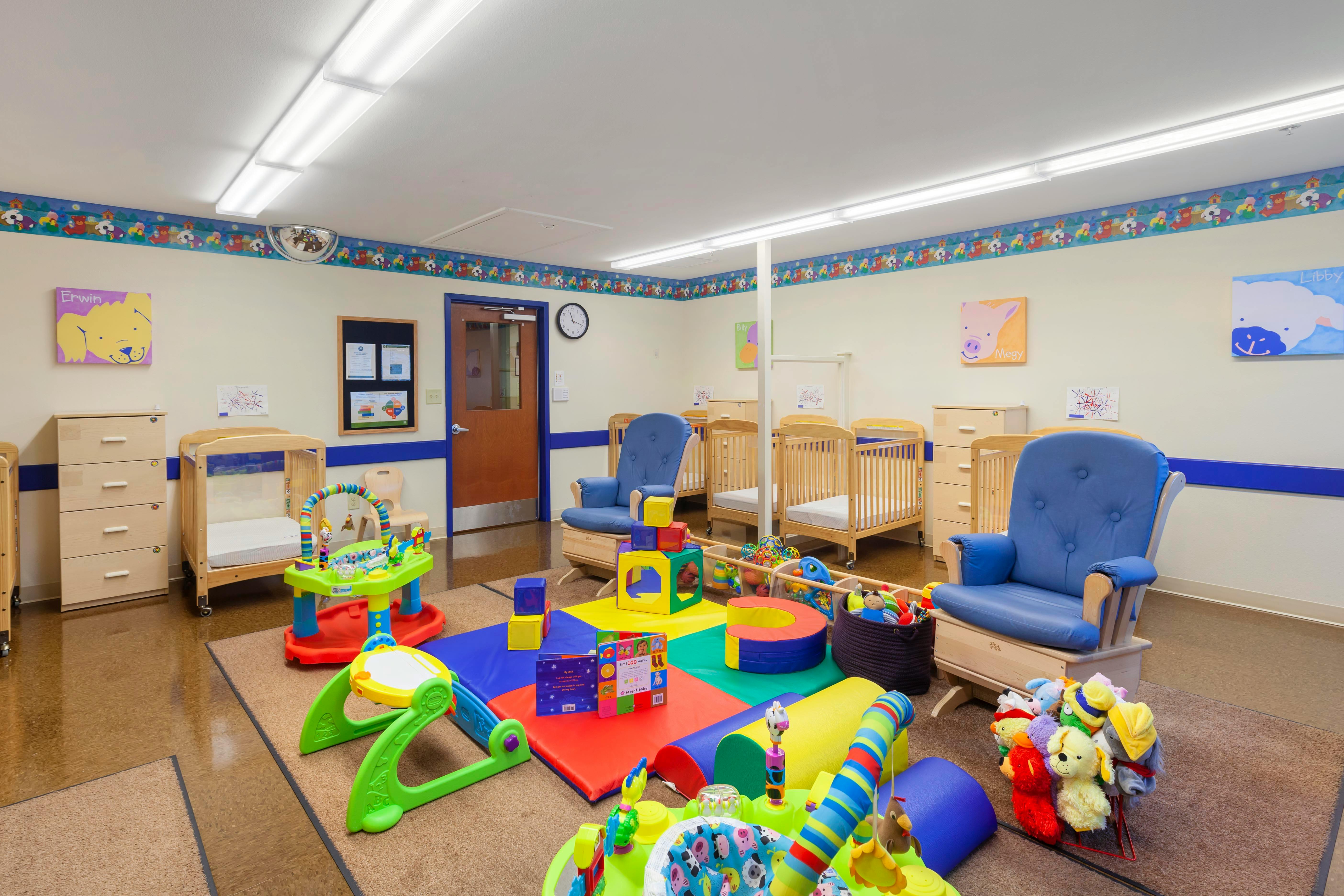 Baby nursery room with cribs, play mats, and a blue rocking chair