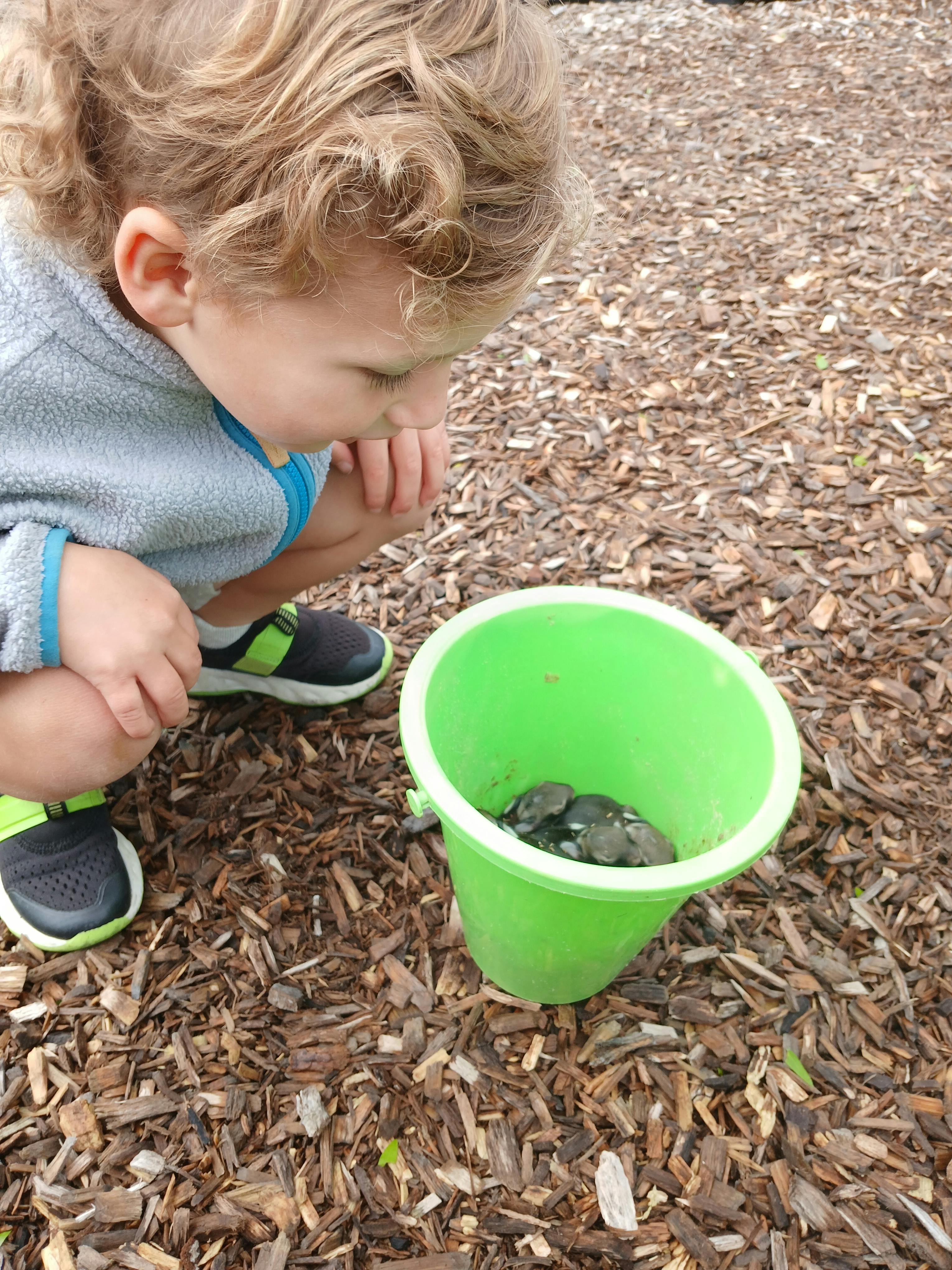 Child kneeling on wood chips with a bucket