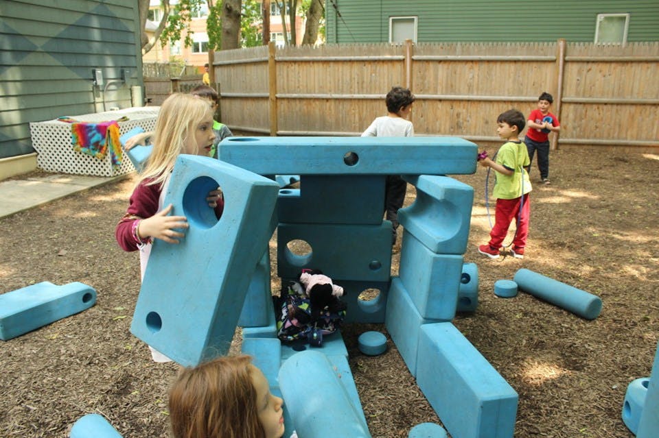 Children playing with large blue building blocks outdoors