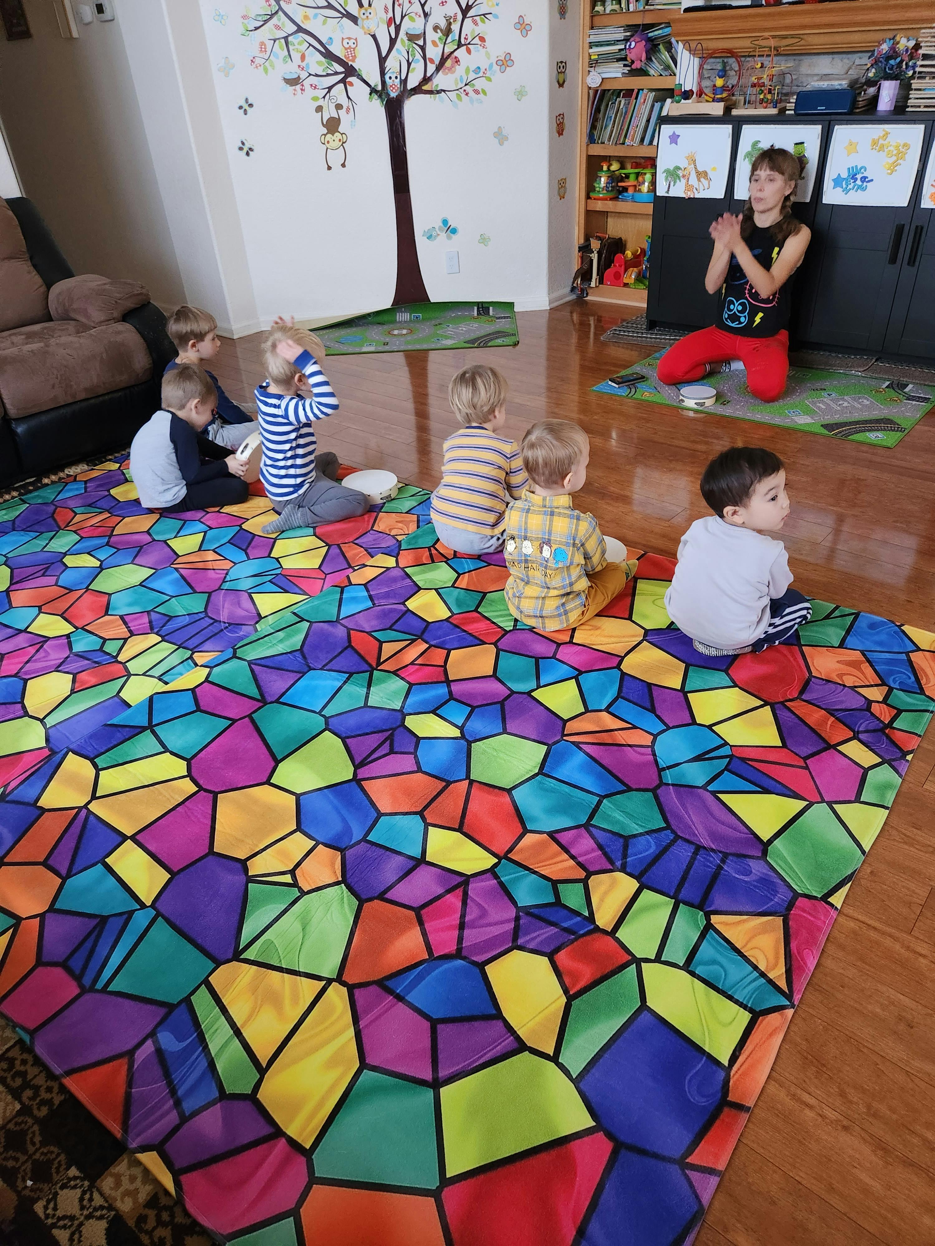 Person kneeling in front of children sitting on a colorful mat