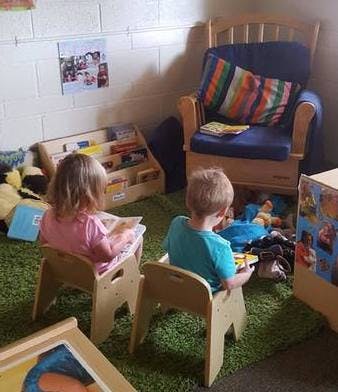 Two children sitting in chairs reading books in a classroom