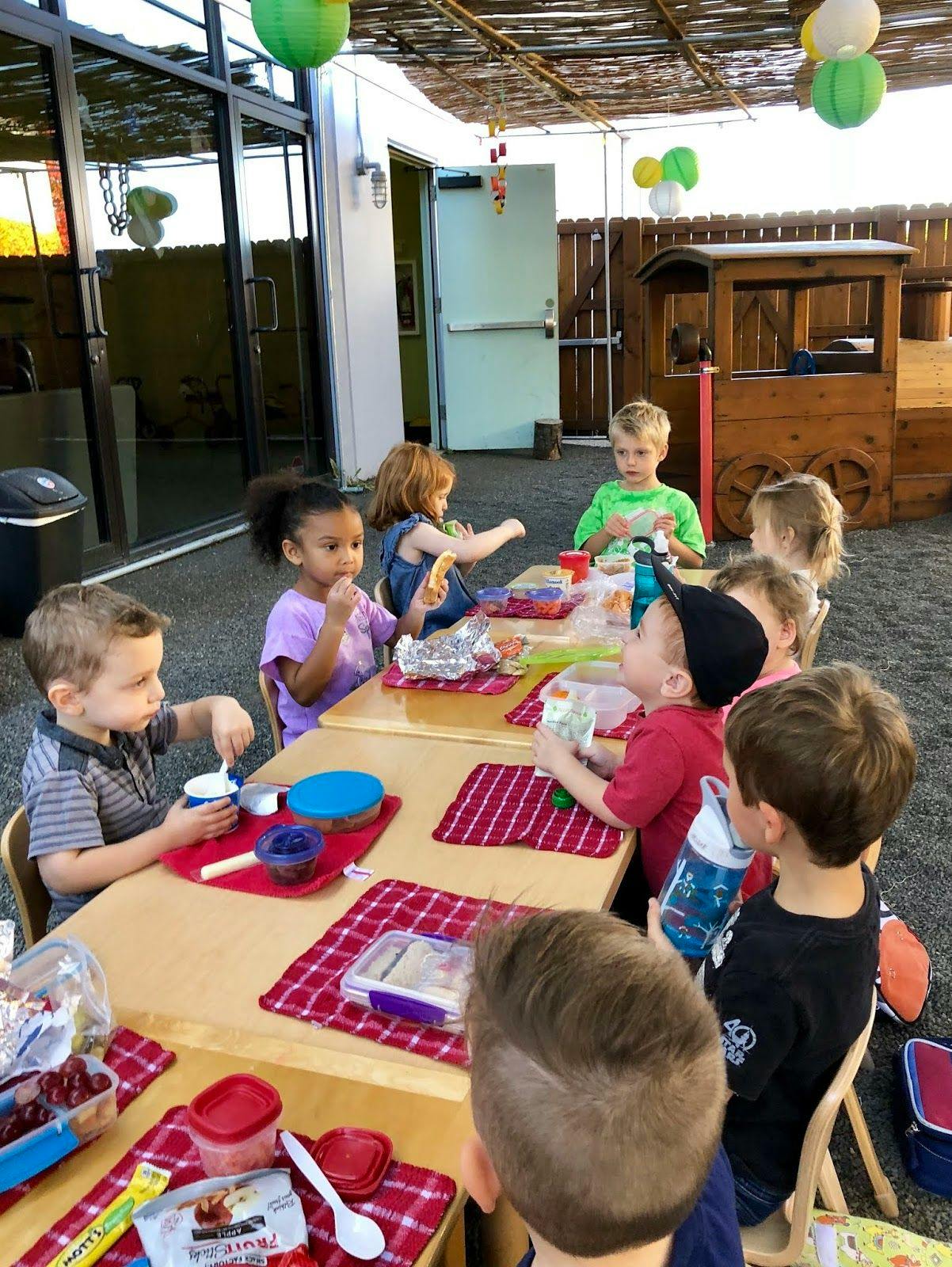 Children sitting at tables eating snacks outdoors