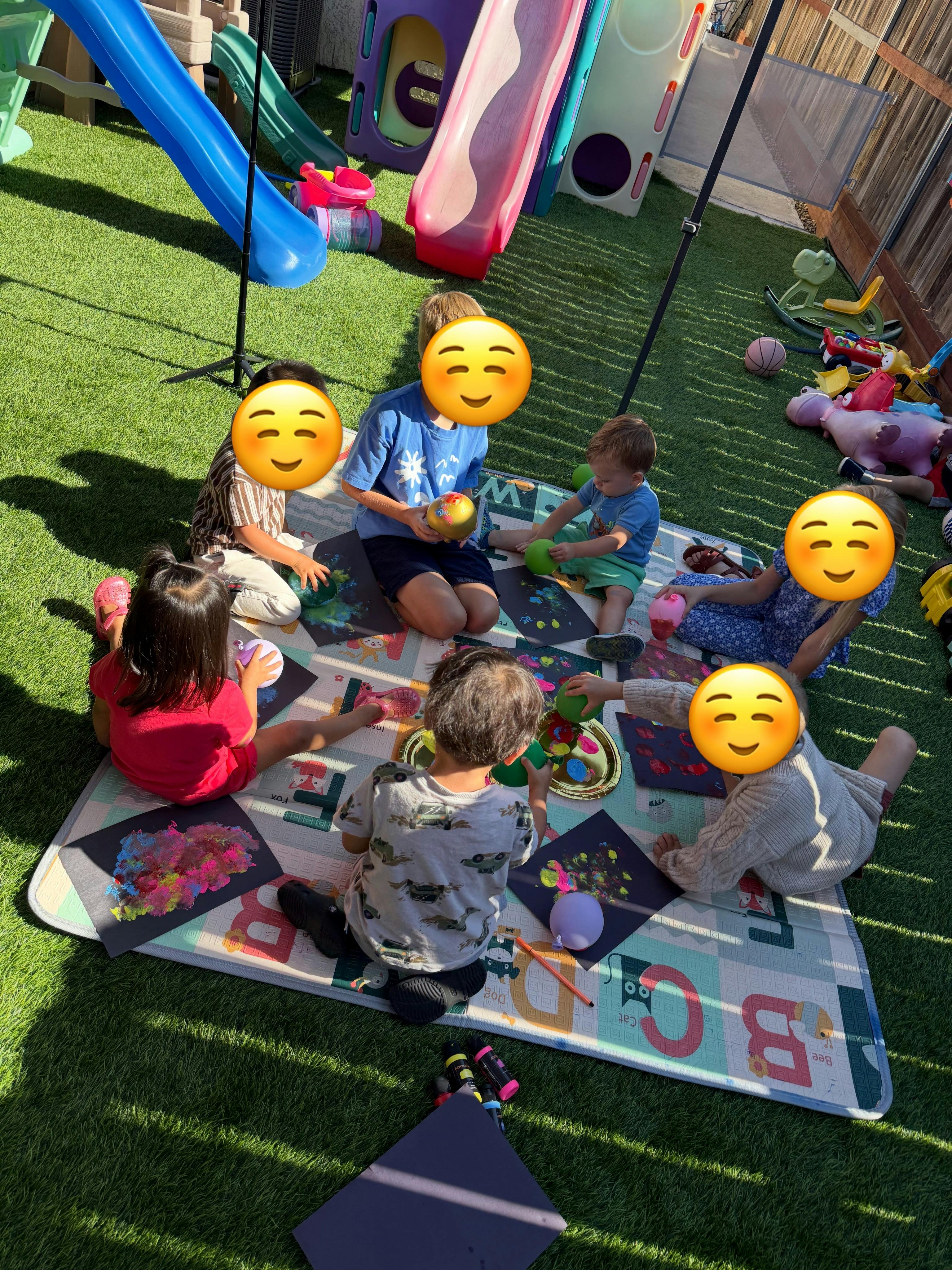Group of children painting with balloons on a mat in a backyard