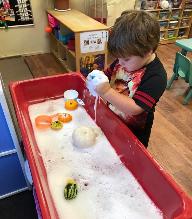 Child playing with bubbles and gourds in a red bin