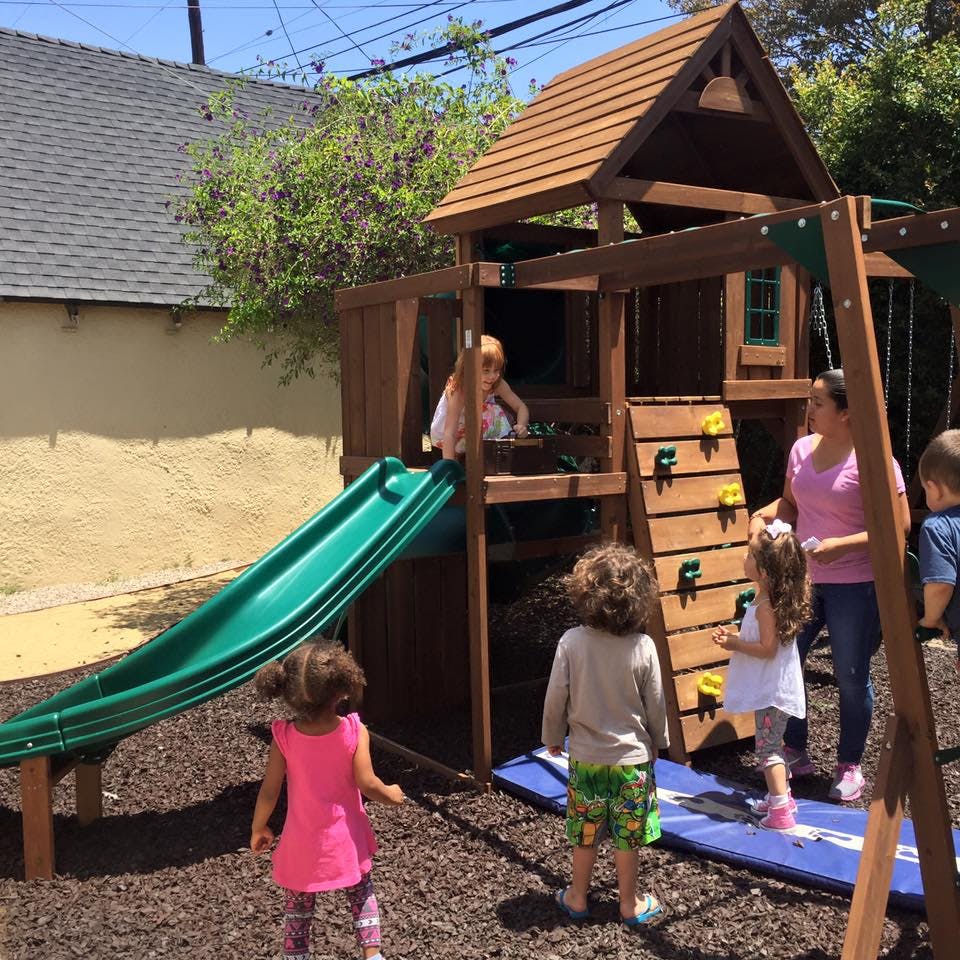 Children and an adult on a playground with a slide and play structure