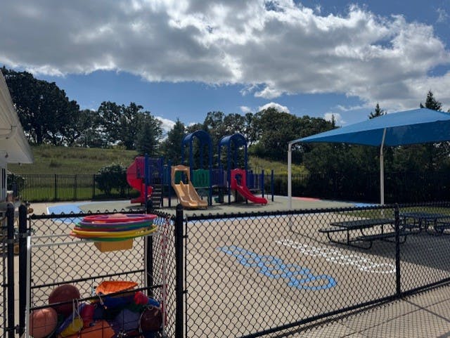 A fenced outdoor playground with slides and swings under a blue sky