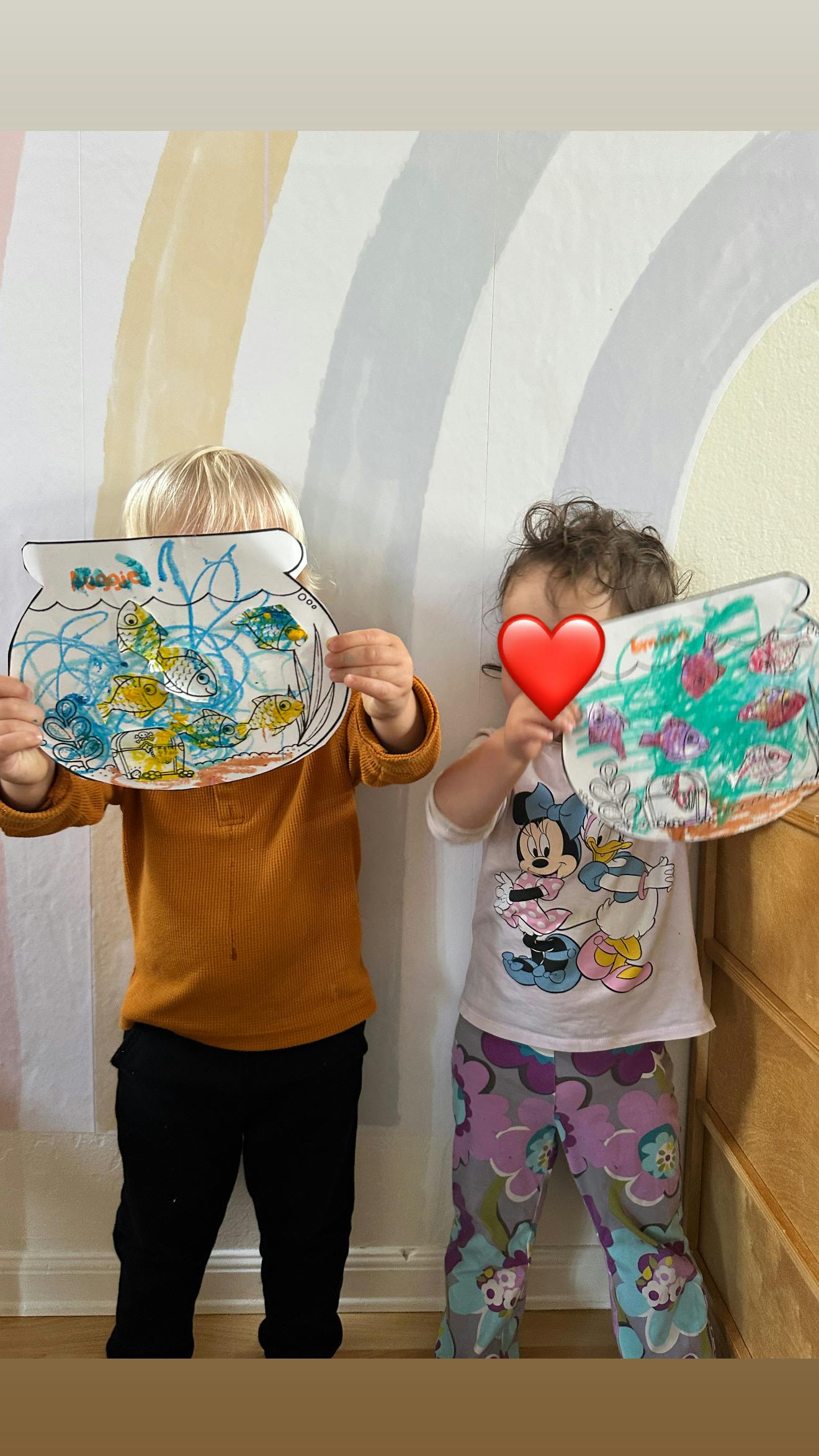 Two children holding up drawings of fishbowls in front of their faces