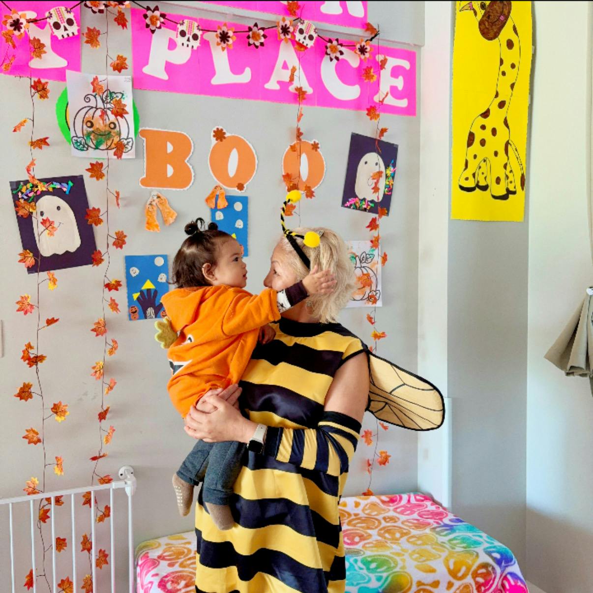 Person in bee costume holding a child in an orange shirt