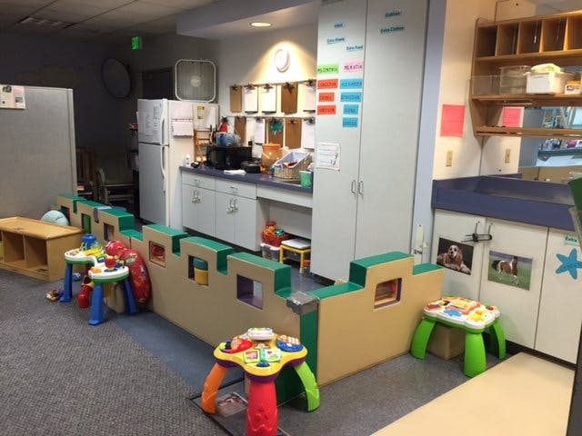 Play area with toy castle wall and small tables in a room with kitchen area in background