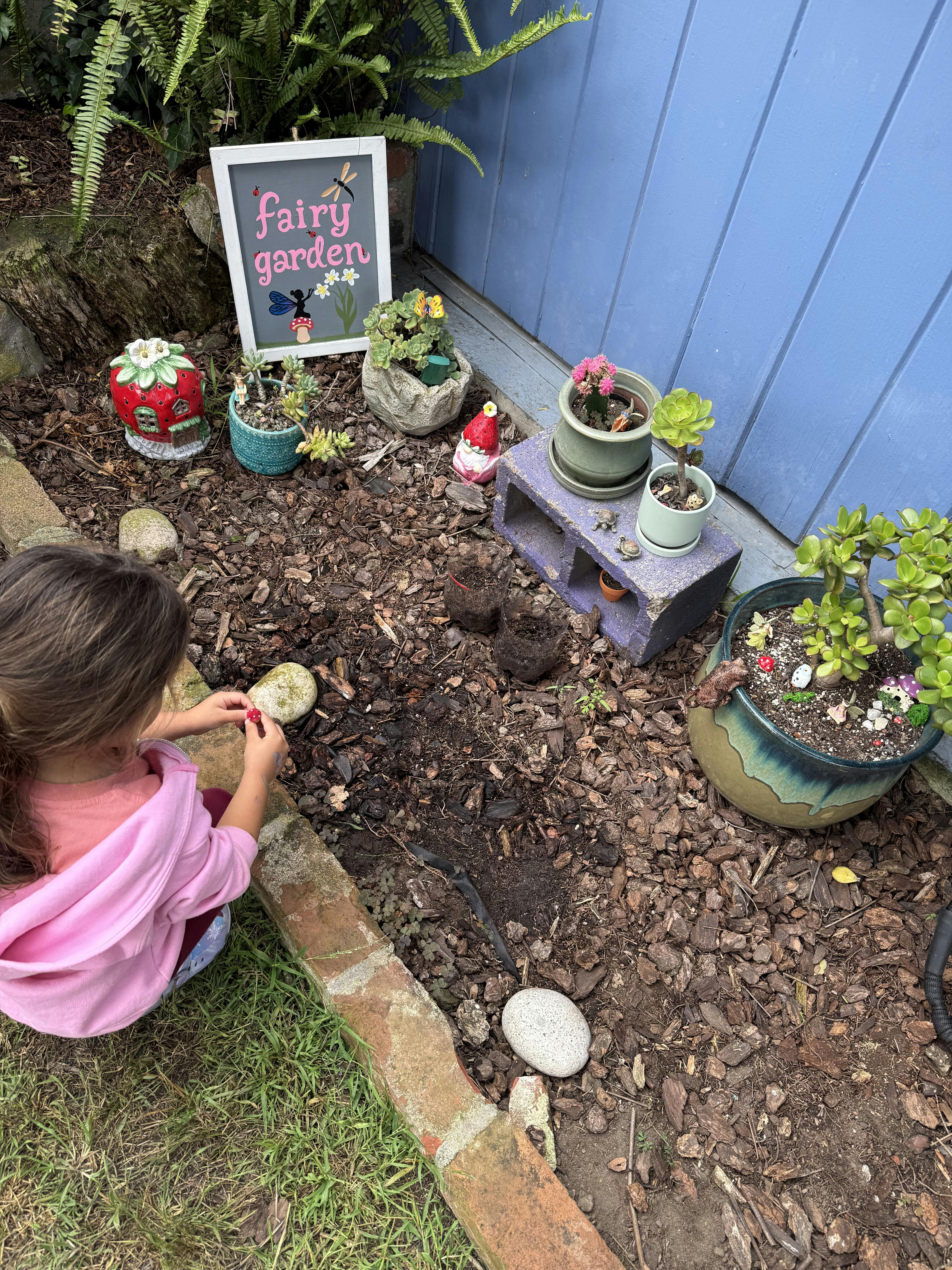 Child playing in a fairy garden with a sign that says "fairy garden"