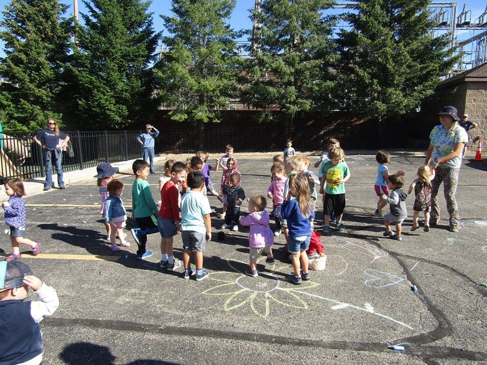 Group of children and adults gathered on pavement with chalk drawings