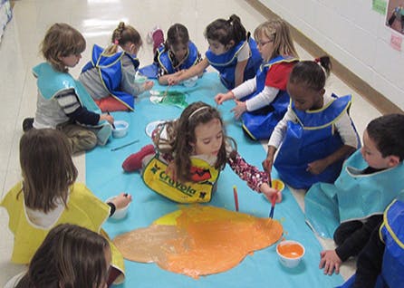 Children painting on a blue mat in a classroom