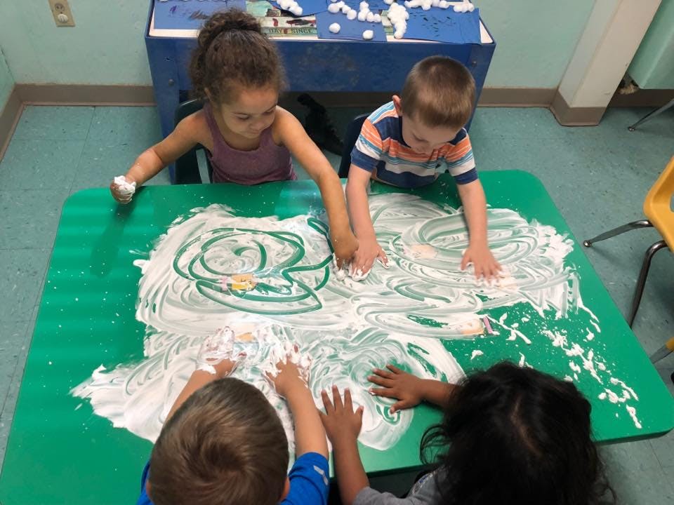 Children playing with shaving cream on a green table