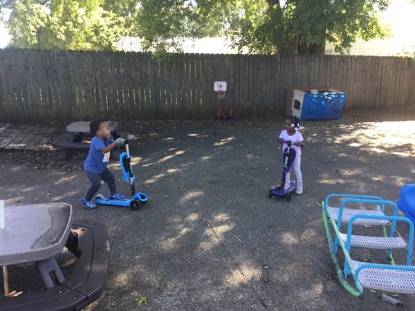 Two children riding scooters in a yard