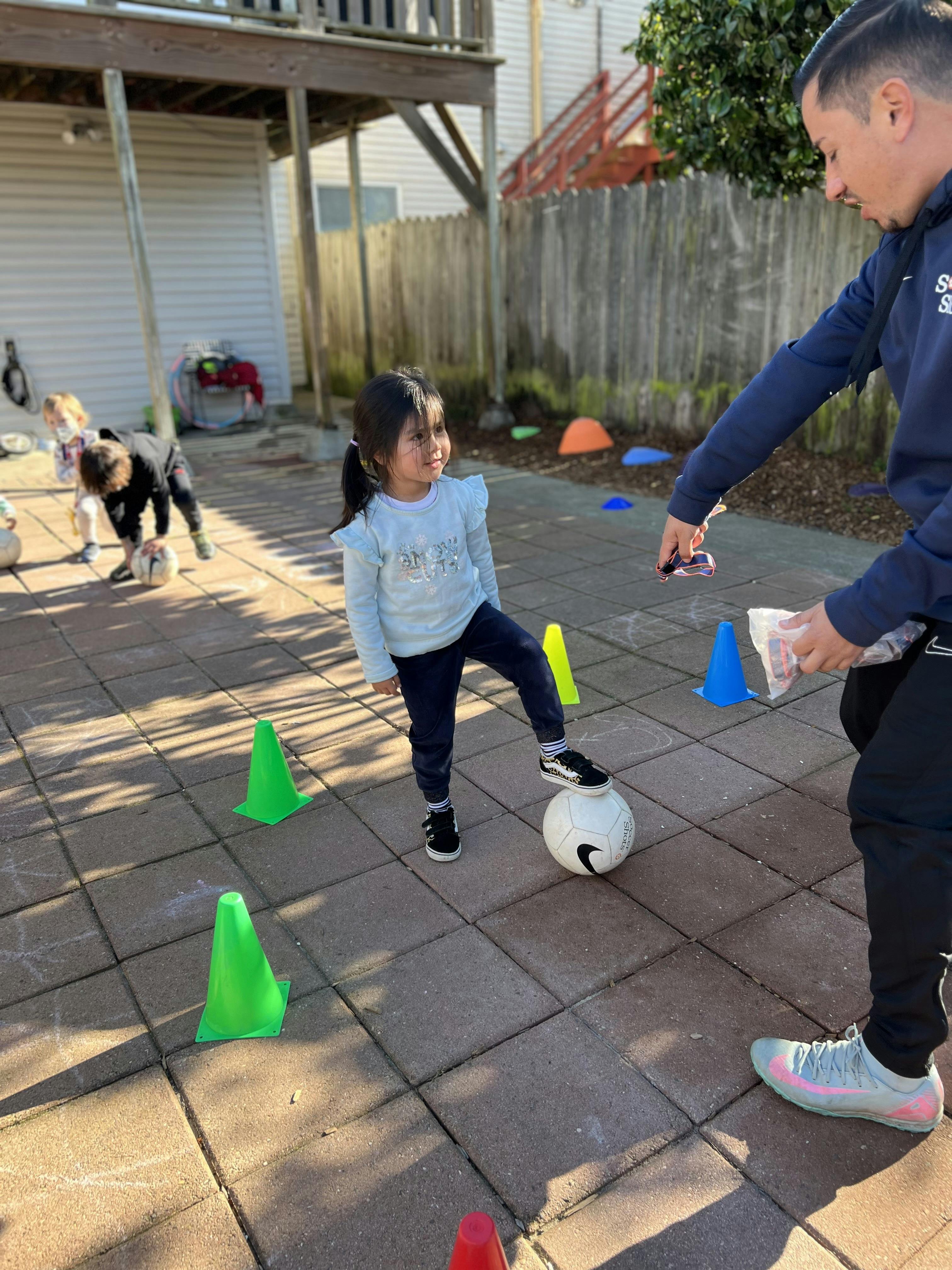 Child with foot on a soccer ball and an adult holding equipment