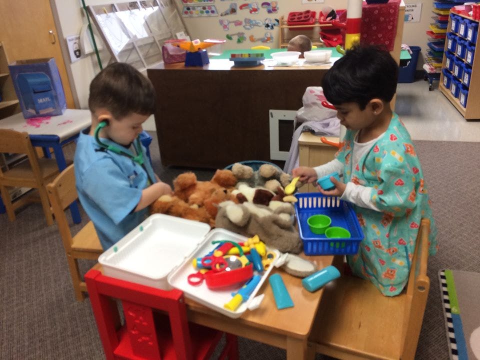 Two children playing with toys and stuffed animals in a classroom