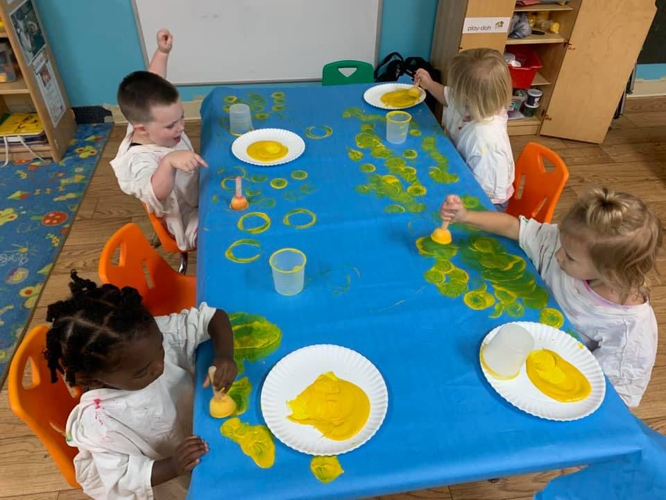 Children painting with yellow paint at a blue table