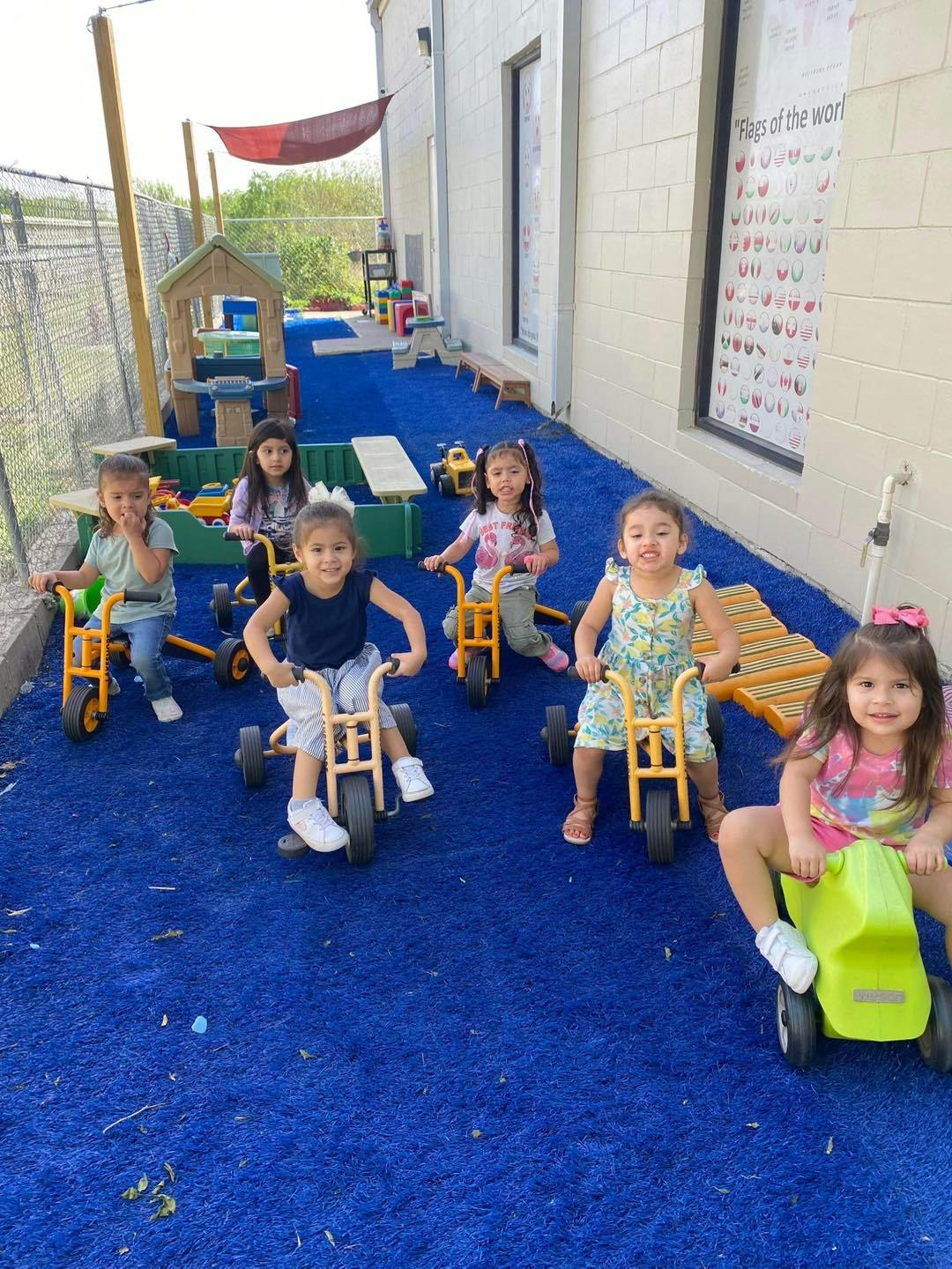 Six children riding tricycles on a blue playground surface