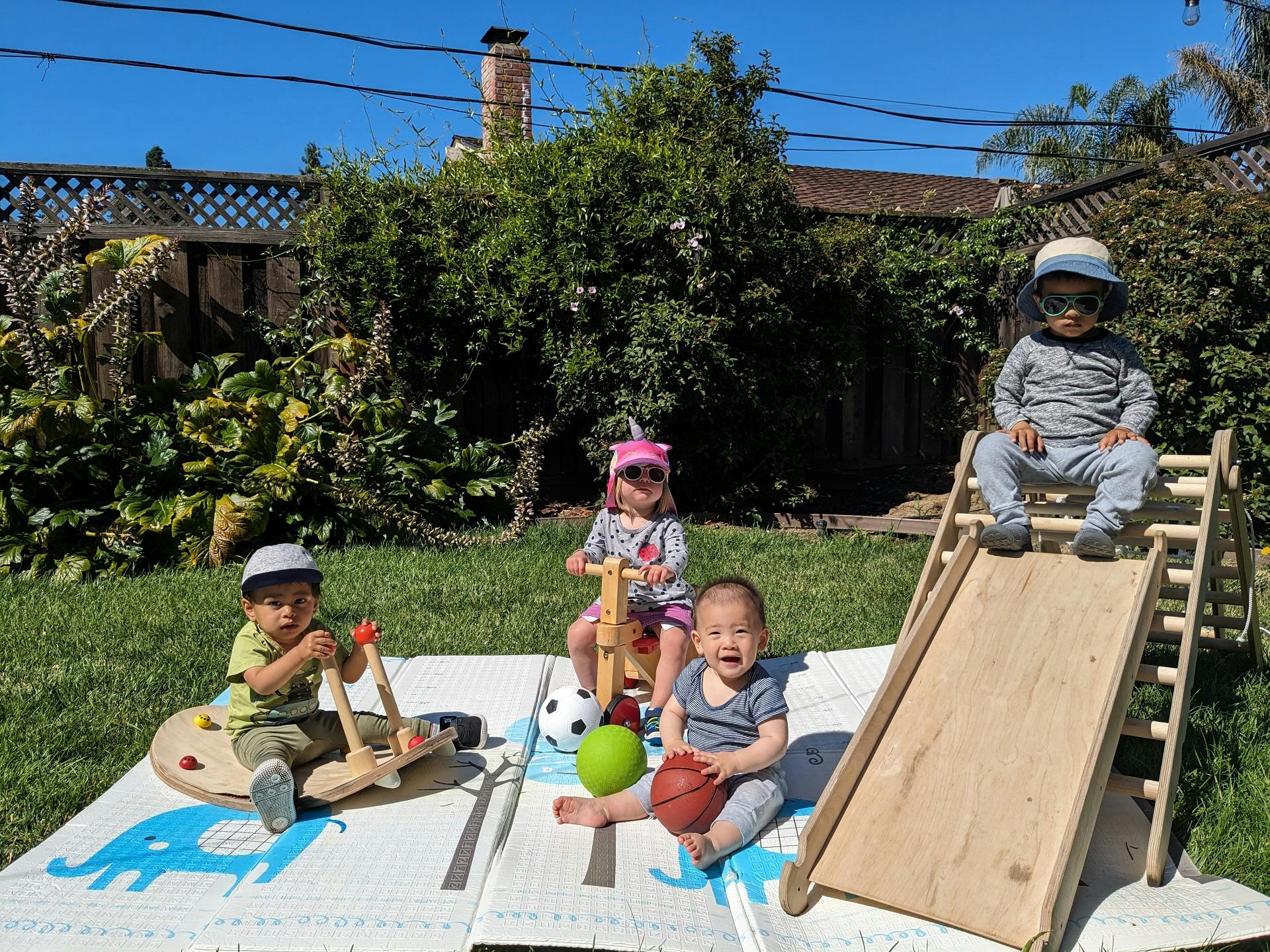 Three children playing with toys on a mat outdoors