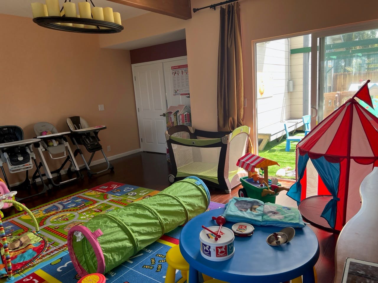 Playroom with a green tunnel, red and blue tent, and high chairs