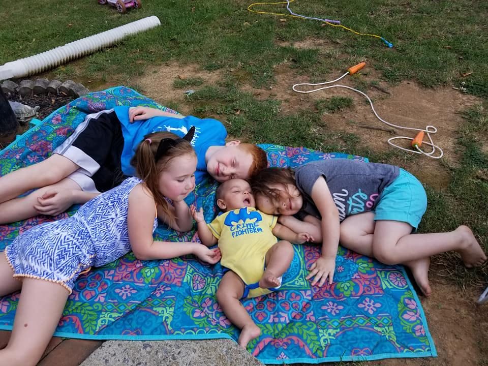 Four children and a baby lying on a blanket on the grass
