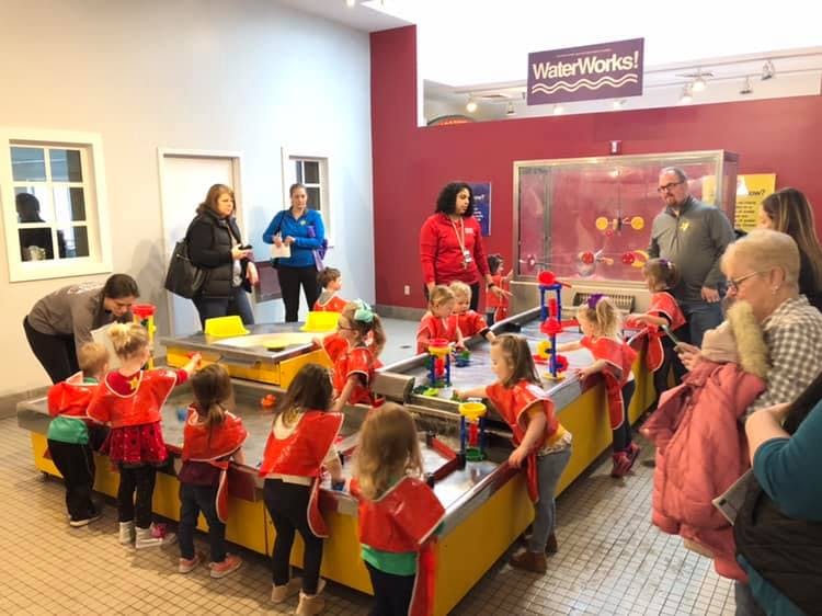 Children and adults interacting with water tables in an indoor play area