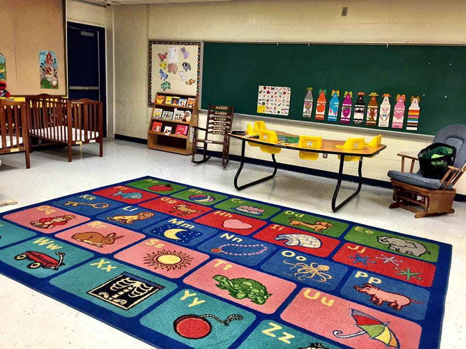 Classroom with alphabet rug, cribs, and chalkboard
