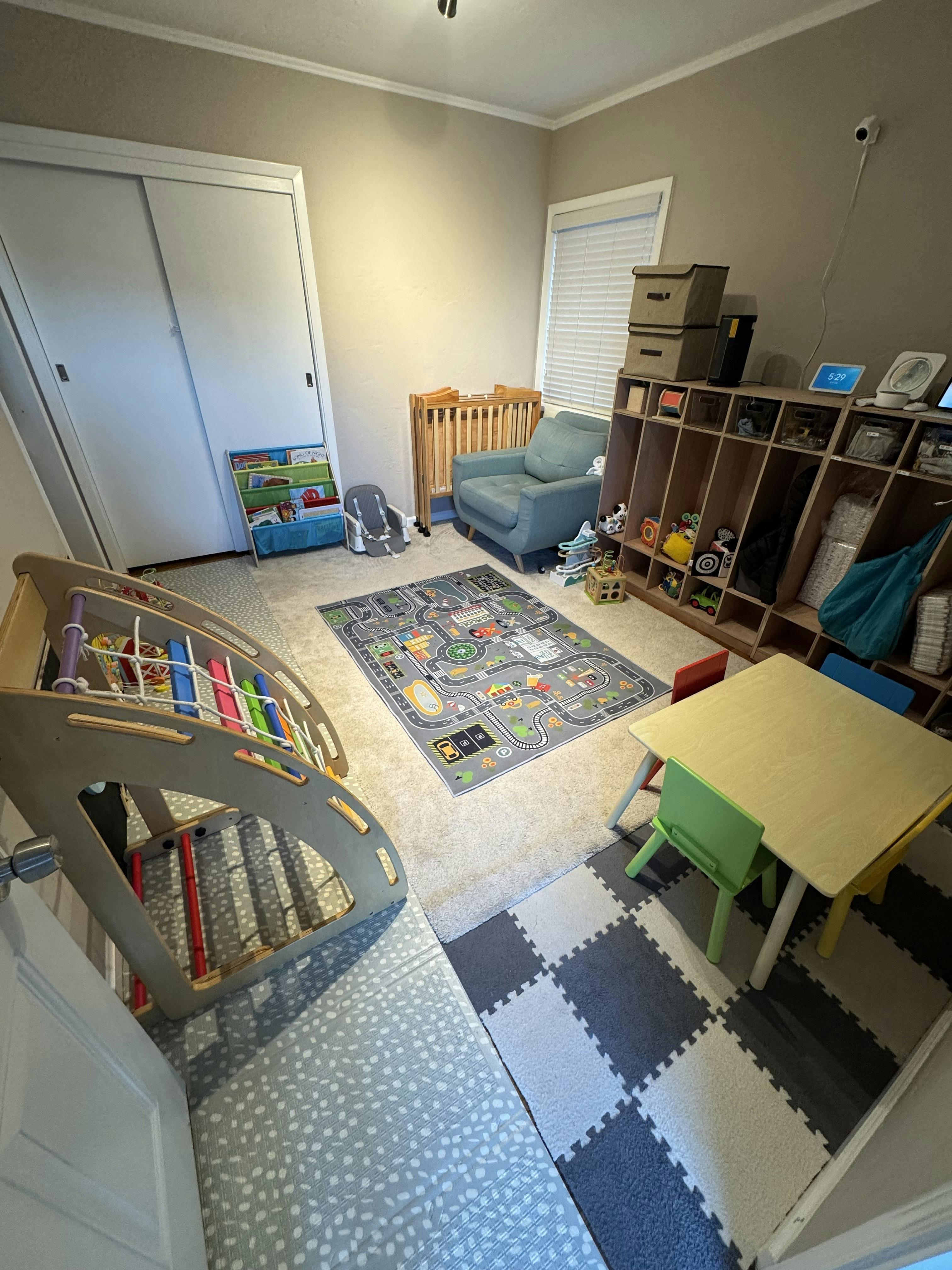 A playroom with a small table and chairs, a road map rug, and shelving with toys