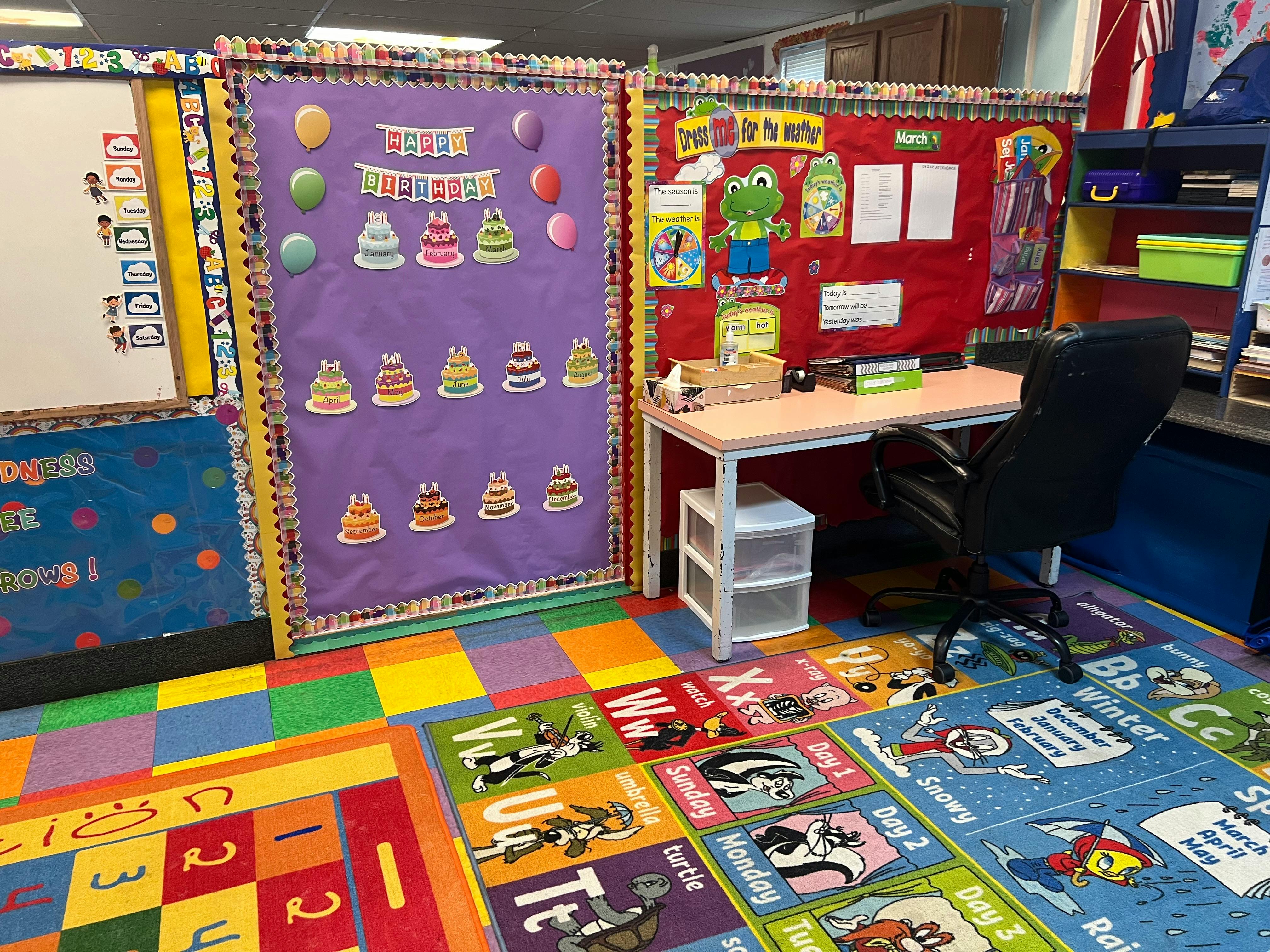 Classroom with colorful rugs, bulletin boards, and a desk with a chair