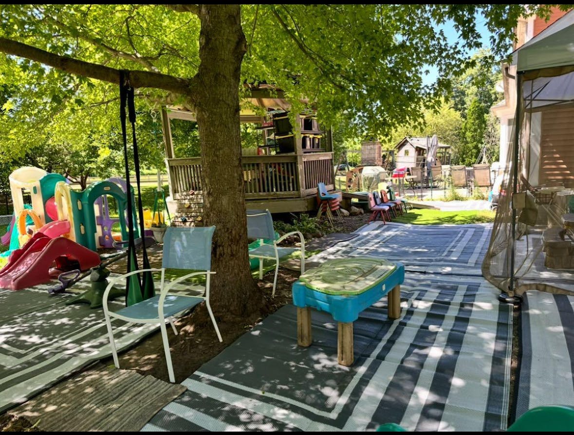 Outdoor play area with slides, swings, chairs, and a small table under a tree