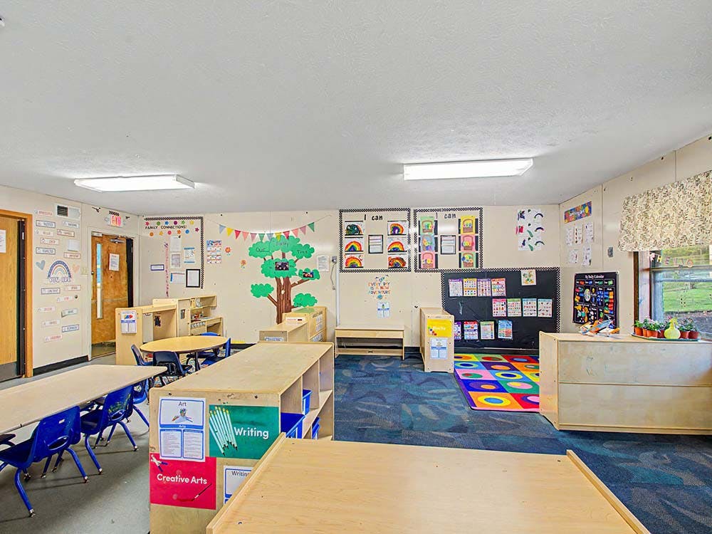 Classroom with tables and chairs, shelves, a colorful rug, and decorated walls