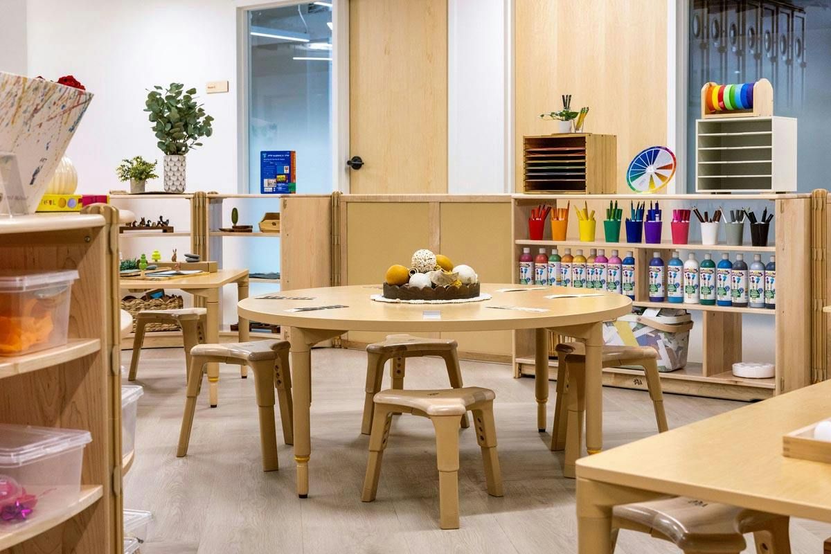 Round table with stools in a classroom with art supplies on shelves