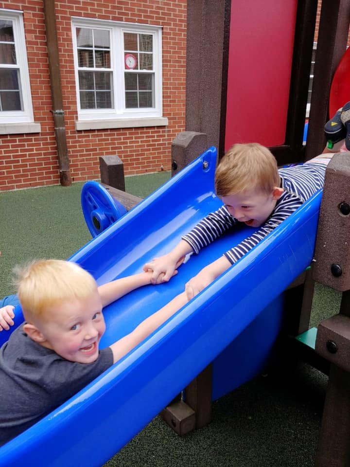 Two children holding hands on a blue slide on a playground