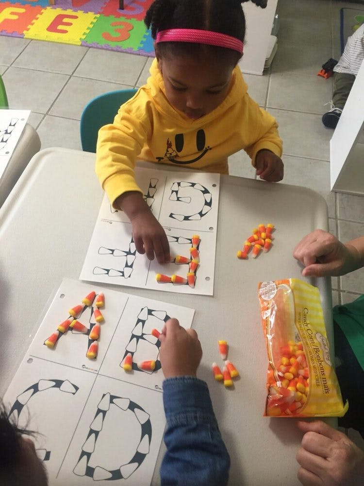 Child and person making letters with candy corn on paper