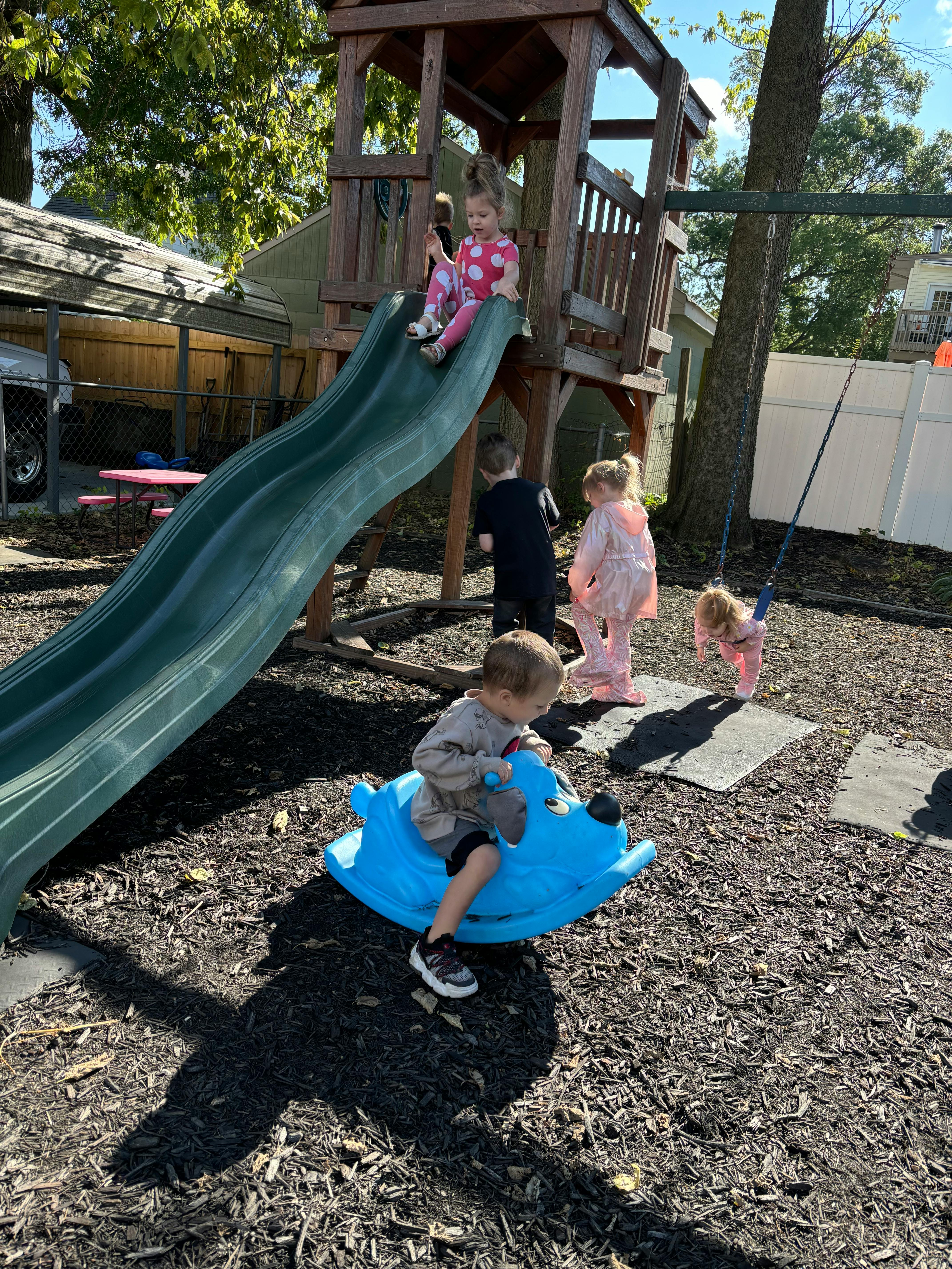 Children playing on a slide, swing, and rocking toy on a playground