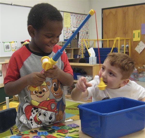 Two children playing with a toy fishing rod and a yellow toy