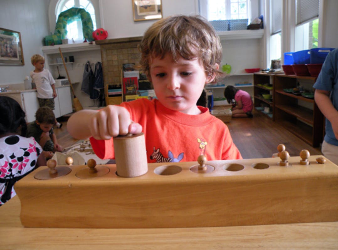 Child playing with a wooden cylinder block in a classroom