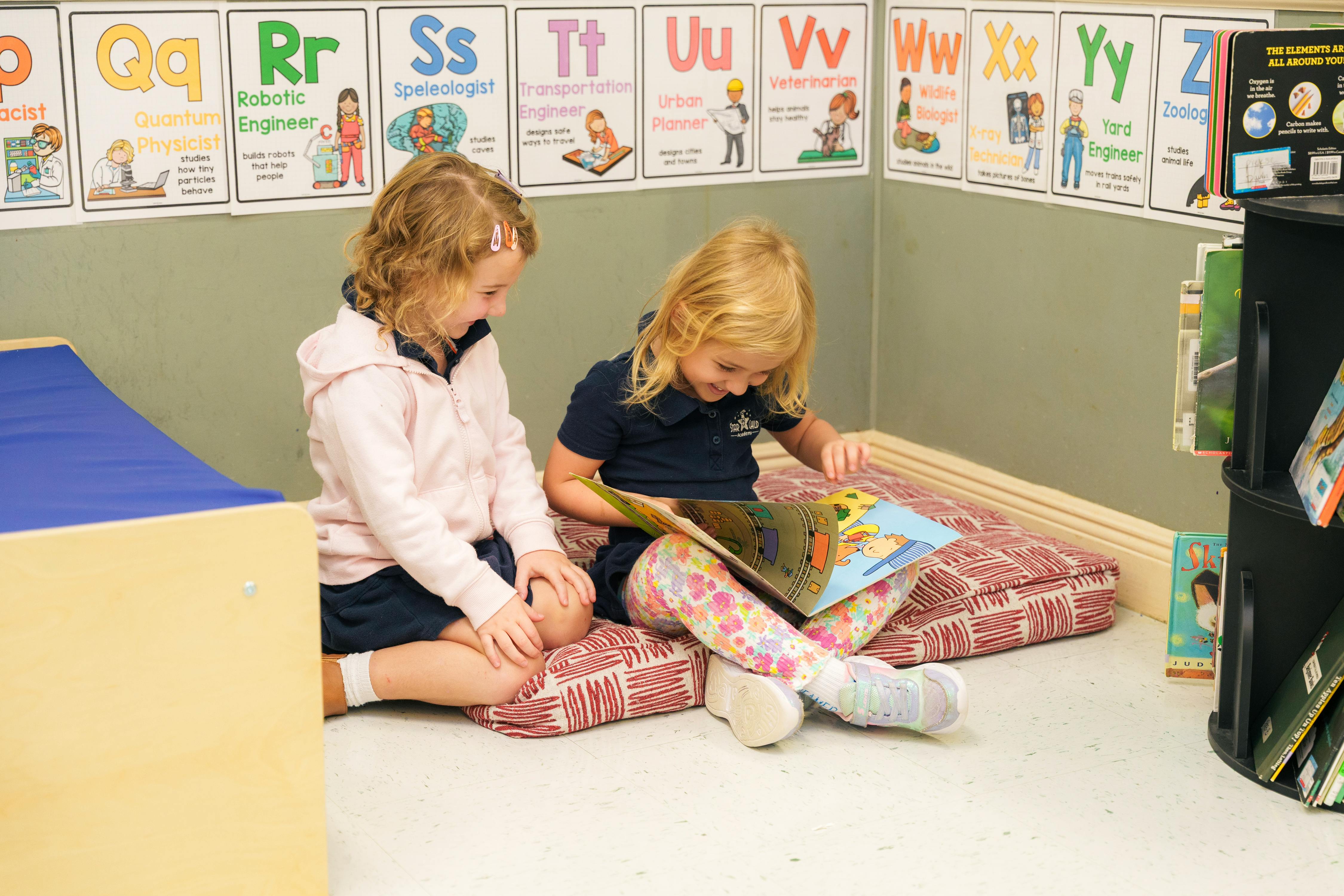 Two children sitting on cushions reading a book in a classroom