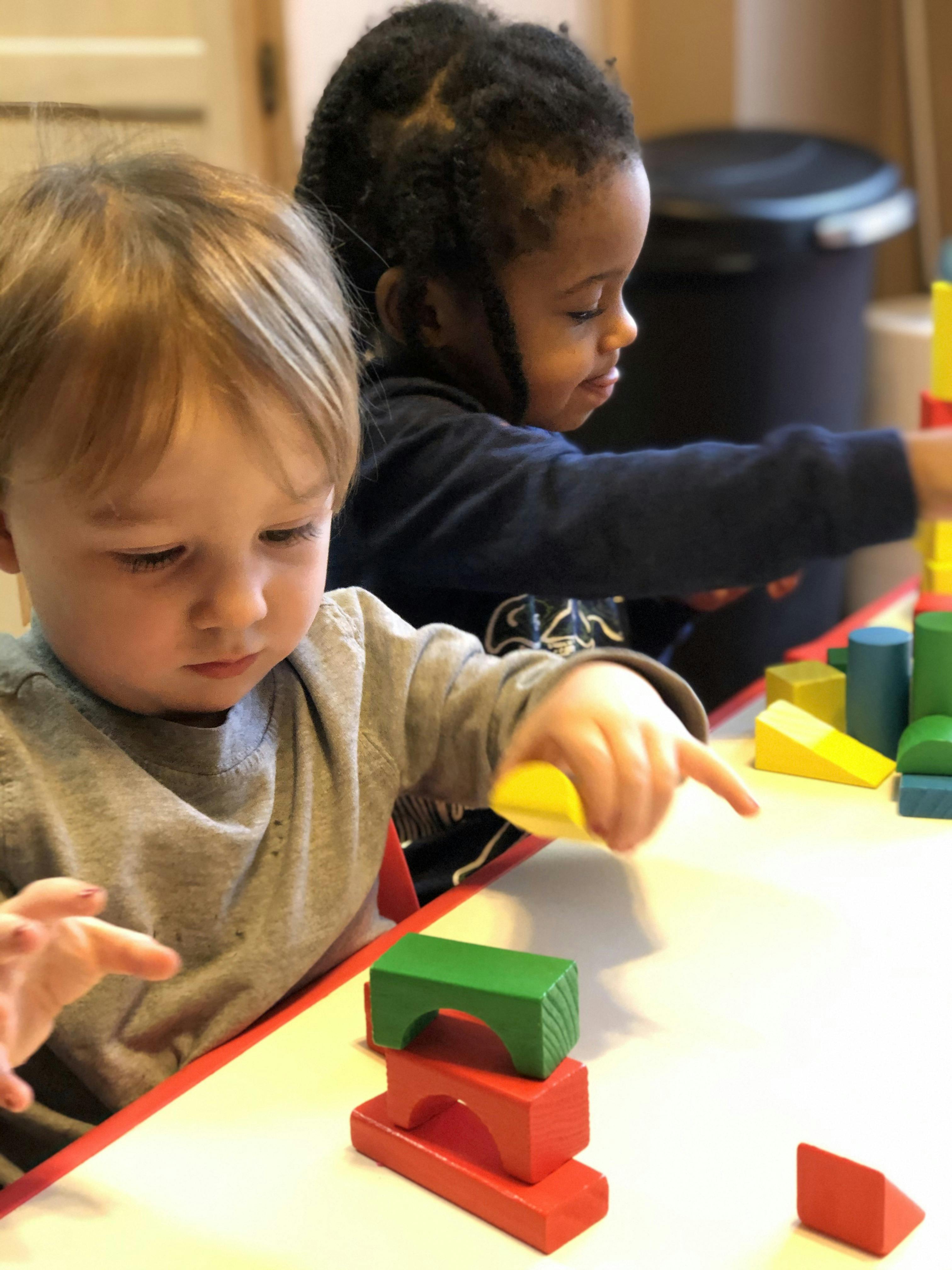 Two children playing with colorful wooden blocks at a table