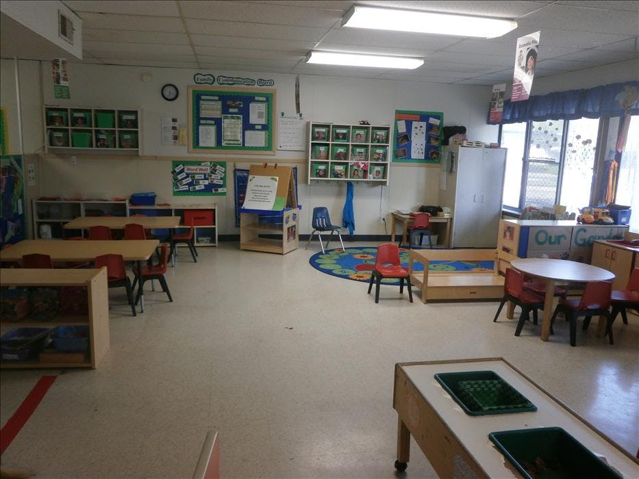 Empty classroom with small tables and chairs, and learning materials on walls and shelves